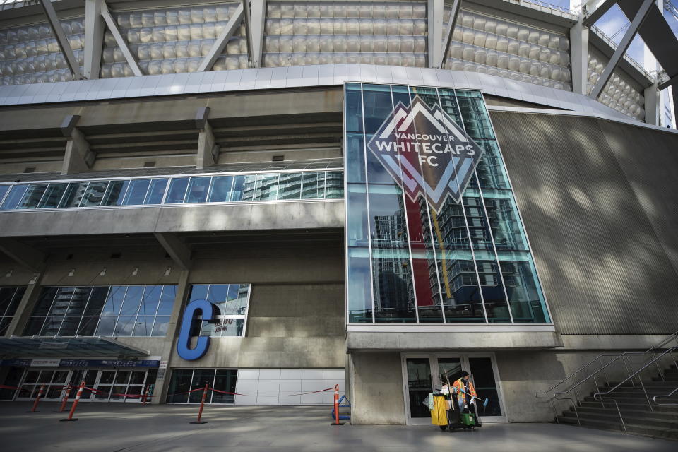 A worker cleans windows and doors at B.C. Place stadium, where Major League Soccer's Vancouver Whitecaps play their home games, in Vancouver, British Columbia, Thursday, March 12, 2020. Major League Soccer is shutting down for 30 days because of the coronavirus, the league announced Thursday. (Darryl Dyck/The Canadian Press via AP)