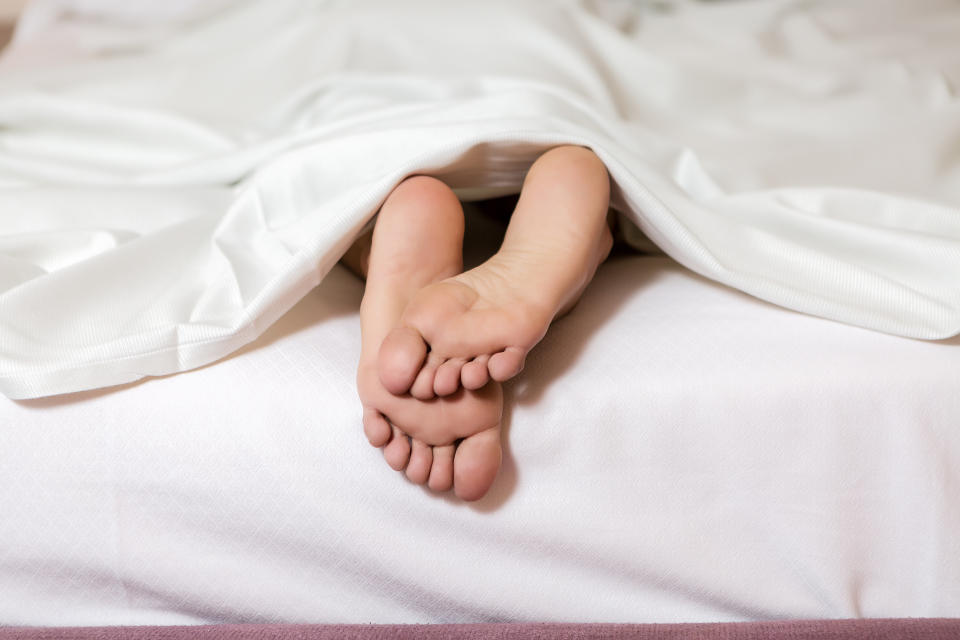 Crop shot of female soft feet lying on white bed under blanket
