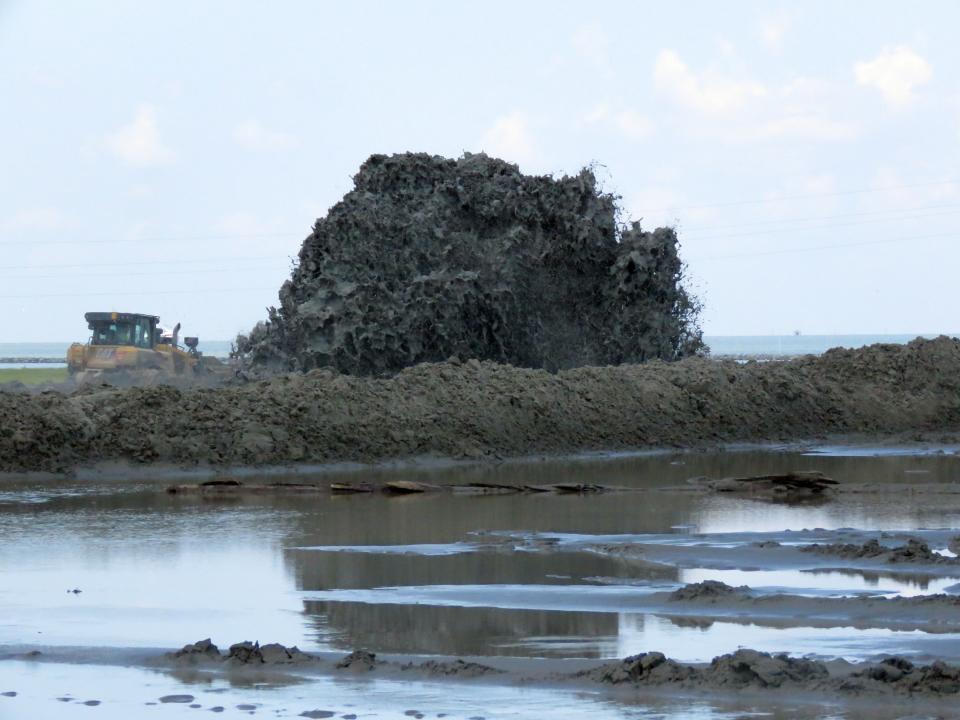 A spray of sand and water being pumped from a dredge five miles away seems to dwarf a bulldozer on a Louisiana barrier island on Wednesday, July 28, 2021. Contractors are at work on a $102 million Louisiana Coastal Restoration and Protection Authority project to add about 400 acres of beach, dune and marshland to Grand Terre Island. Weather permitting, they hope to finish in November. (AP Photo/Janet McConnaughey)