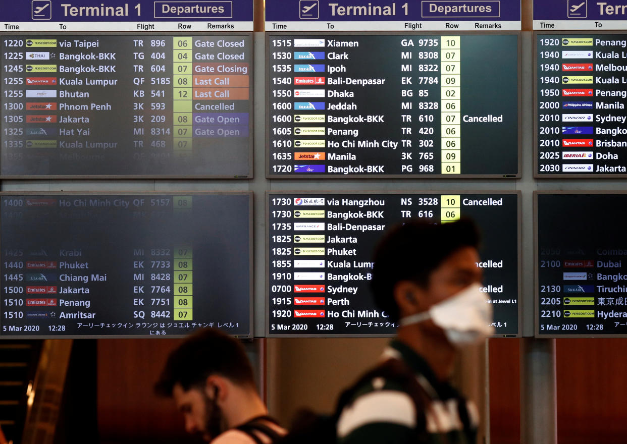 A man wearing a mask passes a flight information board at Changi Airport, following the coronavirus outbreak in Singapore March 5, 2020. REUTERS/Edgar Su