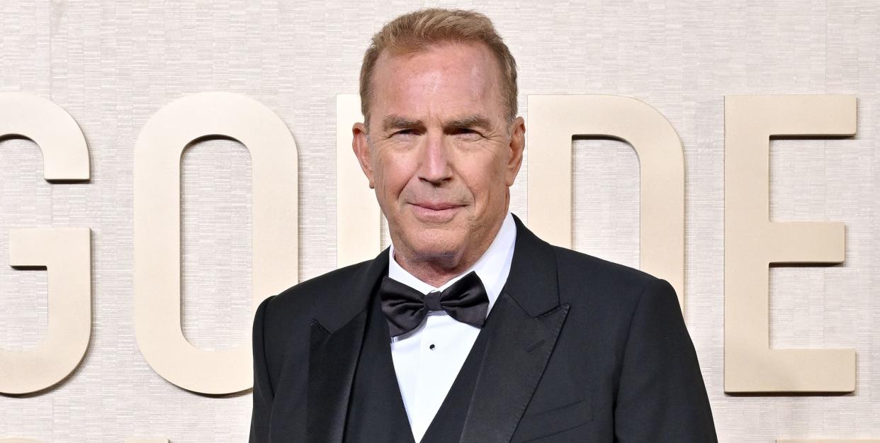 kevin costner, an older man stands looking at the camera with a neutral facial expression, he wears a black suit with bow tie