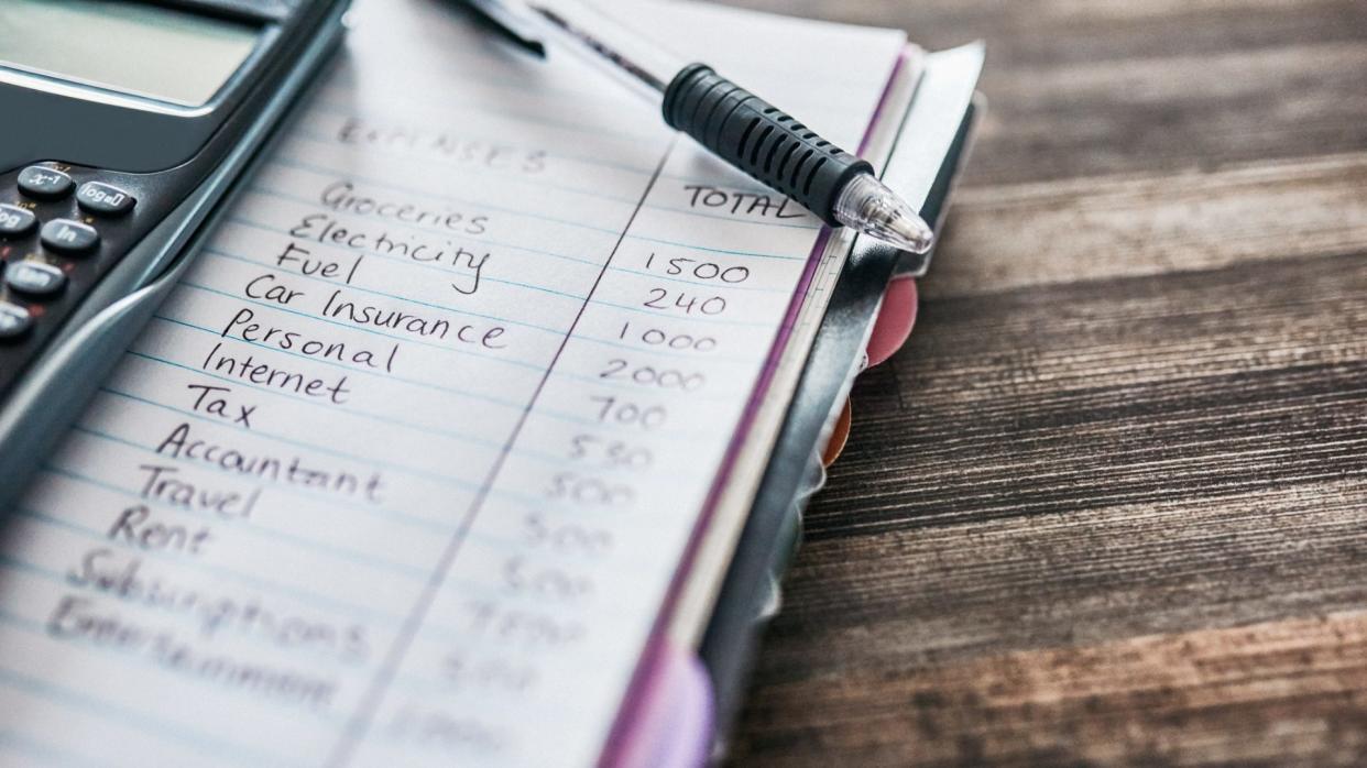 Shot of a notebook with a budget written on it and a calculator on a desk at home.