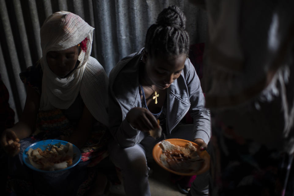 Displaced Tigrayan women, one wearing an Ethiopian Orthodox Christian cross, sit in a metal shack to eat food donated by local residents at a reception center for the internally displaced in Mekele, in the Tigray region of northern Ethiopia, on Sunday, May 9, 2021. (AP Photo/Ben Curtis)