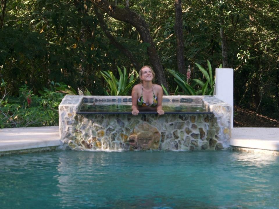A woman in a pool posing for the camera in front of trees.