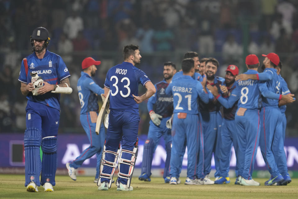 England's Reece Topley and England's Mark Wood look on as Afghanistan's team members celebrate the victory over England by 69 runs in the ICC Men's Cricket World Cup match between Afghanistan and England in New Delhi, India, Sunday, Oct. 15, 2023. (AP Photo/Manish Swarup)