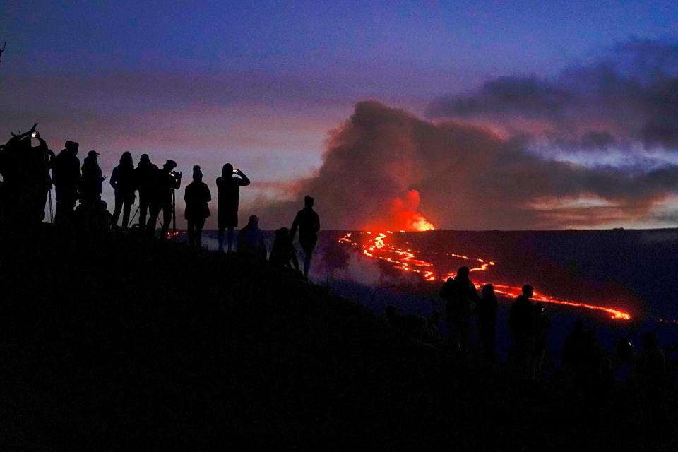 People watch and record images of lava from the Mauna Loa volcano near Hilo, Hawaii. Officials monitoring the Mauna Loa eruption on Hawaii's Big Island said Wednesday that the lava flow moving toward state Route 200 has slowed.