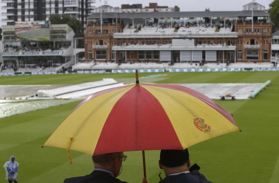Two spectators sit in the stands and look out on the pitch which is covered as rain stops play on day three of the 2nd Ashes Test cricket match between England and Australia at Lord's cricket ground in London, Friday, Aug. 16, 2019. (AP Photo/Alastair Grant)