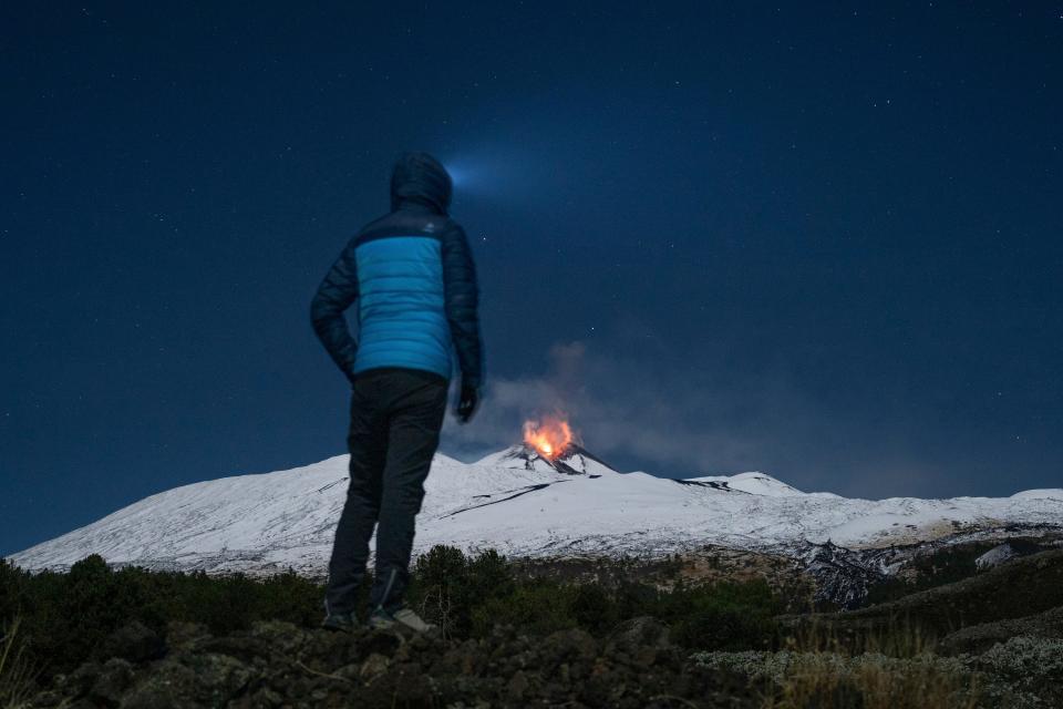 A man is seen watching Mt. Etna from a distance as it spews lava into the sky.