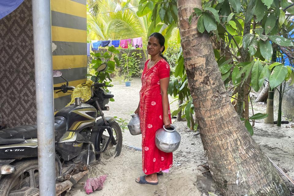 A woman carries pots from a main road to her house in the Chellanam area of Kochi, Kerala state, India, on March 1, 2023. Saltwater's intrusion into freshwater is a growing problem linked to climate change and in Chellanam rising salinity means residents can no longer depend on ponds and wells for the water they need to drink, cook and wash. (Uzmi Athar/Press Trust of India via AP)