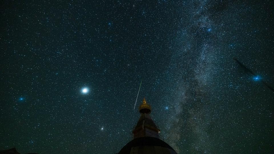 a streak of light zooms between the stars in the night sky