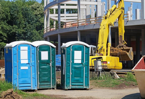 mobile toilets at the construction site next to an excavator, in the background there is the framework of the new building