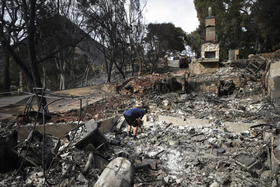 FILE - In this Nov. 13, 2018 file photo Roger Kelton searches through the remains of his mother-in-law's home leveled by the Woolsey Fire, in the southern California city of Agoura Hills. A Southern California utility has agreed to pay $360 million to settle lawsuits brought by cities, counties and other public agencies over deadly wildfires sparked by its equipment in the last two years, including one that was later blamed for a mudslide that killed more than 20 people. An attorney for 23 public entities said Wednesday, Nov. 13, 2019, that Southern California Edison has agreed to the sum to repay taxpayers for firefighting and damage from the Thomas Fire in 2017 and Woolsey Fire last year. (AP Photo/Jae C. Hong,File)