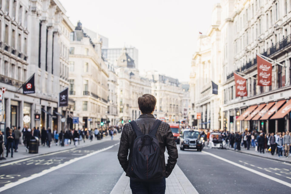 A man wearing a backpack and walking in the middle of a city street