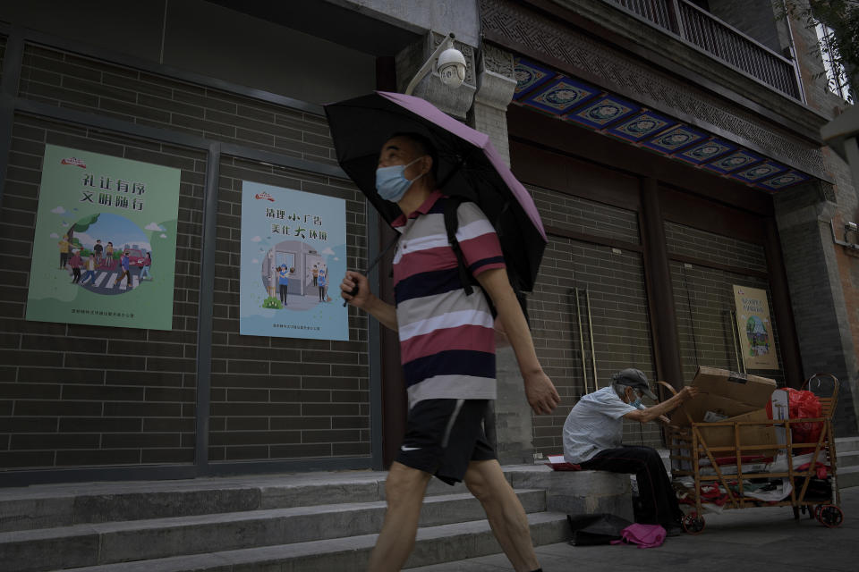 A man wearing a face mask and holding an umbrella to shield from the sunlight as he walks by an elderly man collecting recycle items in front of vacant shop lots at Qianmen Street in Beijing, Wednesday, Aug. 17, 2022. Factories in China's southwest have shut down after reservoirs used to generate hydropower ran low in a worsening drought, adding to economic strains at a time when President Xi Jinping is trying to extend his position in power. (AP Photo/Andy Wong)