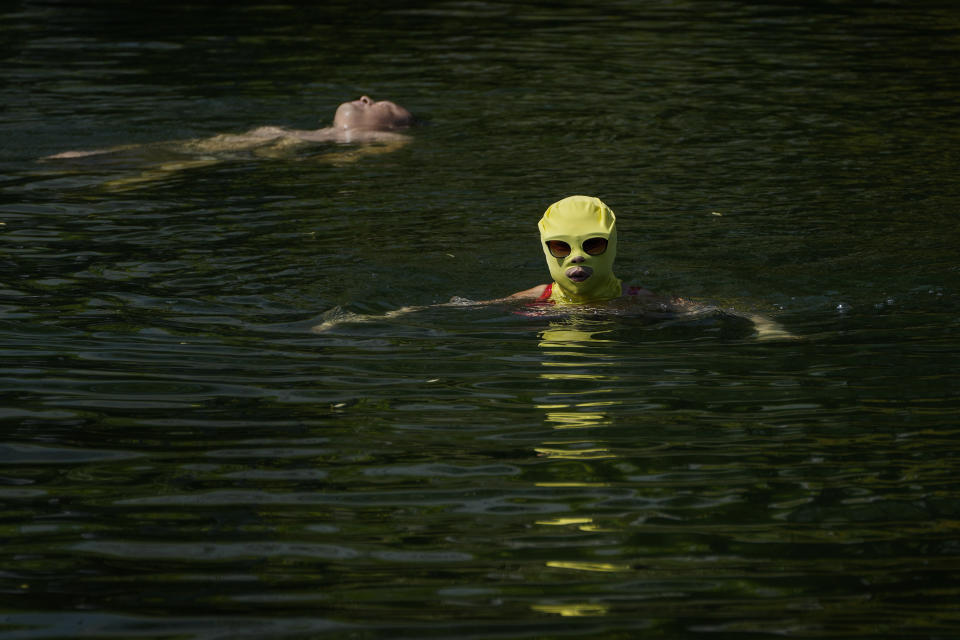 A woman wearing a sun protection headgear and wearing a sun glasses swims as residents cool off on a sweltering day at an urban waterway in Beijing, Monday, July 10, 2023. Rescuers were looking Monday for several people missing in a landslide triggered by torrential rains while employers across much of China were ordered to limit outdoor work due to scorching temperatures as the country struggled with heat, flooding and drought. (AP Photo/Andy Wong)