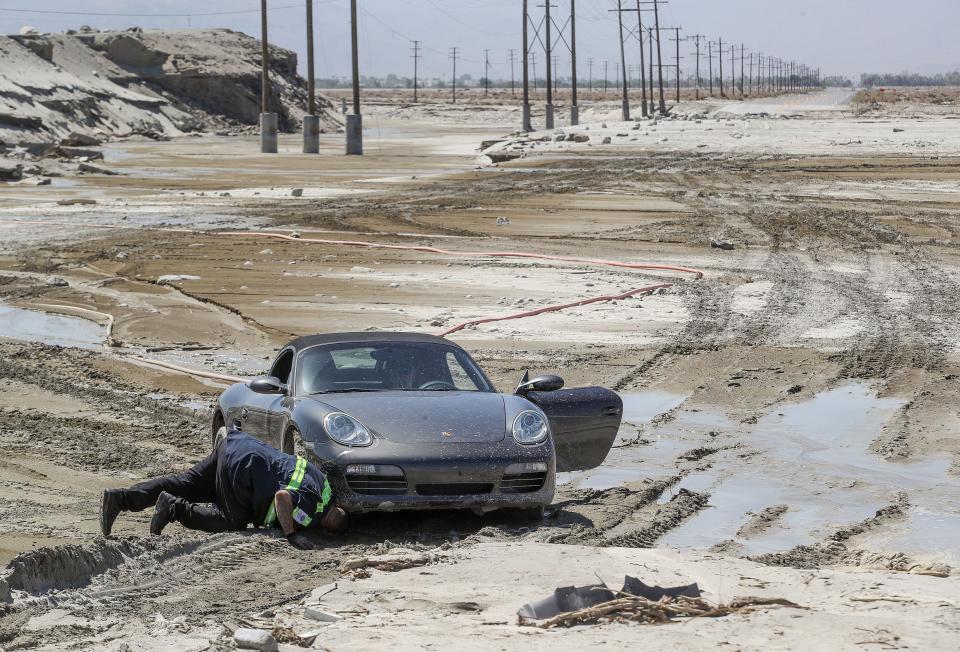 A tow truck driver works to free two people who drove through the barriers and became stuck in the mud on Indian Canyon Dr. at the Whitewater River in Palm Springs, Calif., August 24, 2023.