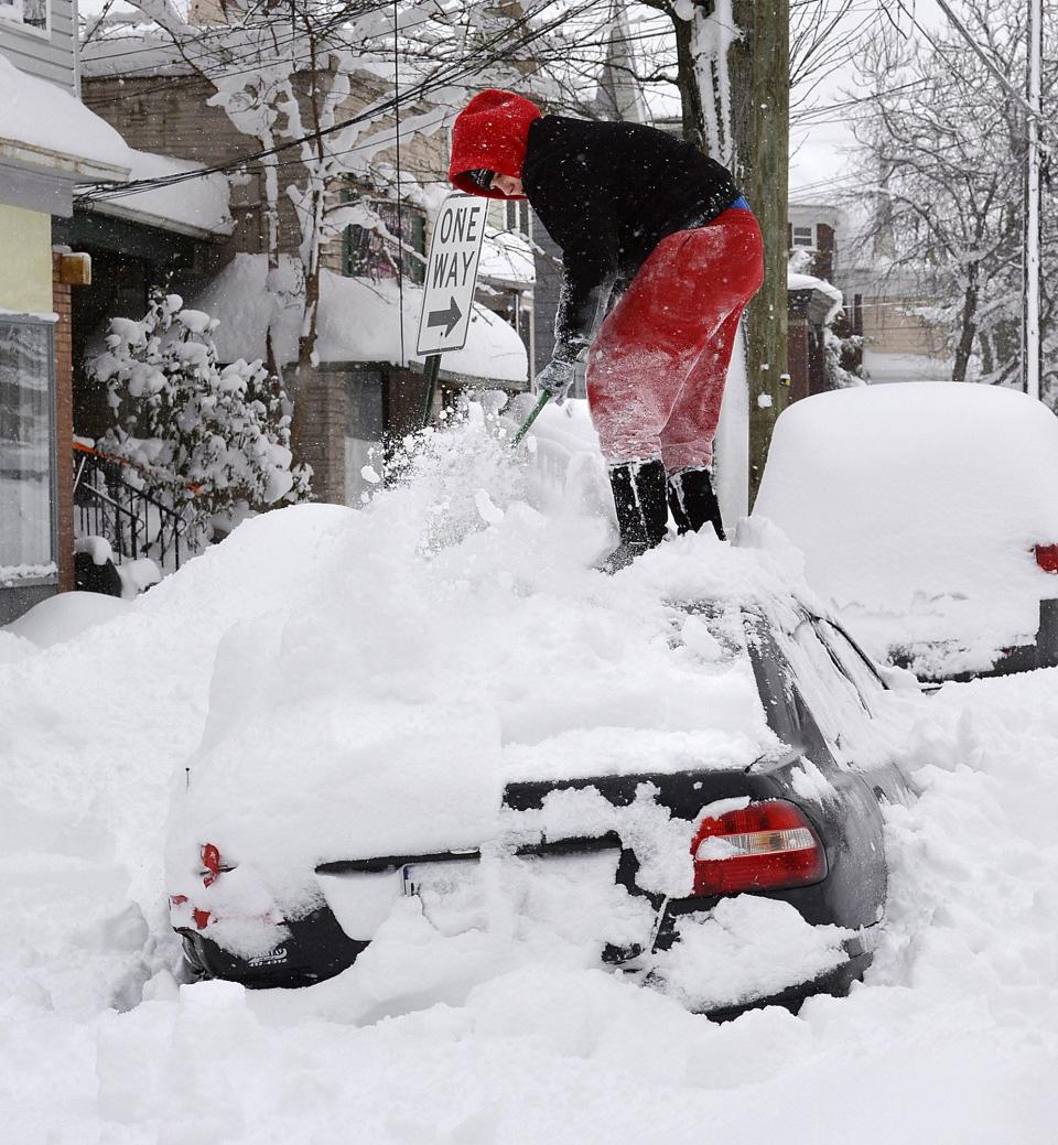 Erie resident Soledda Hernandez stands on the roof of her car as she brushes off snow near West Eighth and Liberty streets in Erie on Dec. 27, 2017.