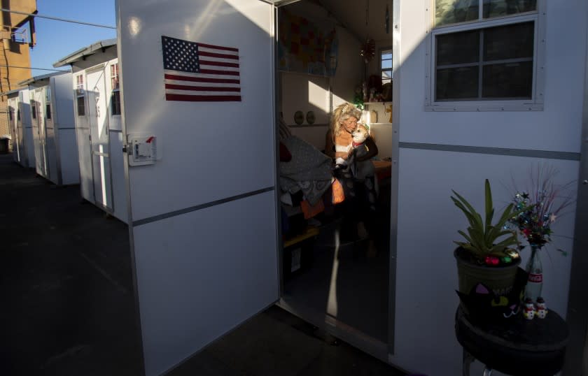 RIVERSIDE, CA - NOVEMBER 30, 2020: Karen Morea, 62, hugs her dog Jack-Jack inside her tiny village home in a parking lot adjacent to a Riverside shelter on November 30, 2020 in Riverside, California. She has been here almost two months after living on the streets. Los Angeles is embracing the idea of tiny homes to get homeless off the streets, but the buildings are sitting in storage.(Gina Ferazzi / Los Angeles Times)