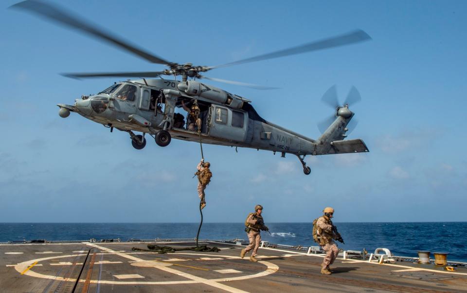 Marines descend by rope from an MH-60S Sea Hawk helicopter to board the USS Bainbridge