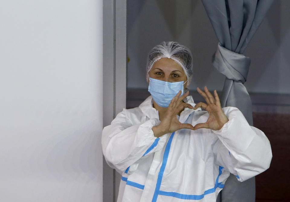 A medical worker wearing protective gear gestures as people wait to receive the COVID-19 vaccine, at Belgrade Fair makeshift vaccination center, in Belgrade, Serbia, Monday, Jan. 25, 2021. Serbia were the first European country to receive the Chinese Sinopharm's vaccine for mass inoculation programmes. (AP Photo/Darko Vojinovic)