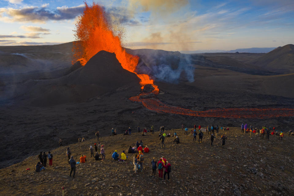 People watch as lava flows from an eruption from the Fagradalsfjall volcano on the Reykjanes Peninsula in southwestern Iceland on Tuesday, May 11, 2021. The glow from the bubbling hot lava spewing out of the Fagradalsfjall volcano can be seen from the outskirts of Iceland's capital, Reykjavík, which is about 32 kilometers (20 miles) away. Pandemic or no pandemic, the world will never stand still. That's perhaps no clearer than in Iceland where the Fagradalsfjall volcano has awoken from a slumber that has lasted 6,000 years, give or take a year or two. (AP Photo/Miguel Morenatti)