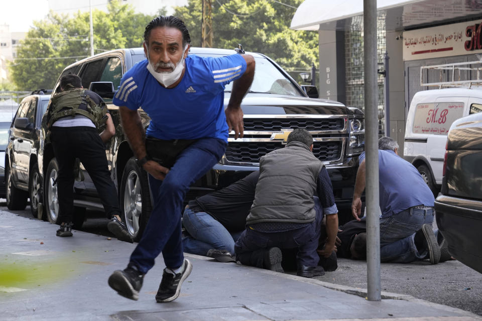 A man runs to take cover as supporters of a Shiite group allied with Hezbollah help injured men during armed clashes that erupted during a protest in the southern Beirut suburb of Dahiyeh, Lebanon, Thursday, Oct. 14, 2021. It was not immediately clear what triggered the gunfire, but tensions were high along a former civil war front-line between Muslim Shiite and Christian areas. (AP Photo/Hassan Ammar)