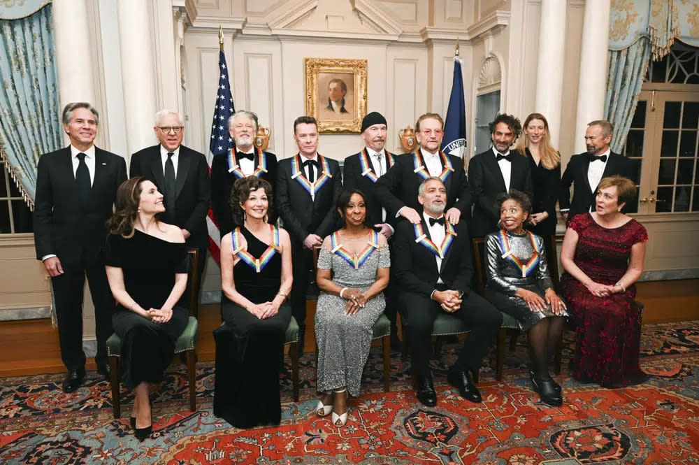 2022 Kennedy Center Honoree George Clooney, bottom third from right, reacts as he is given a shoulder rub from fellow 2022 Honoree Bono during a group photo at the State Department following the Kennedy Center Honors gala dinner, Saturday, Dec. 3, 2022, in Washington. (AP Photo/Kevin Wolf)