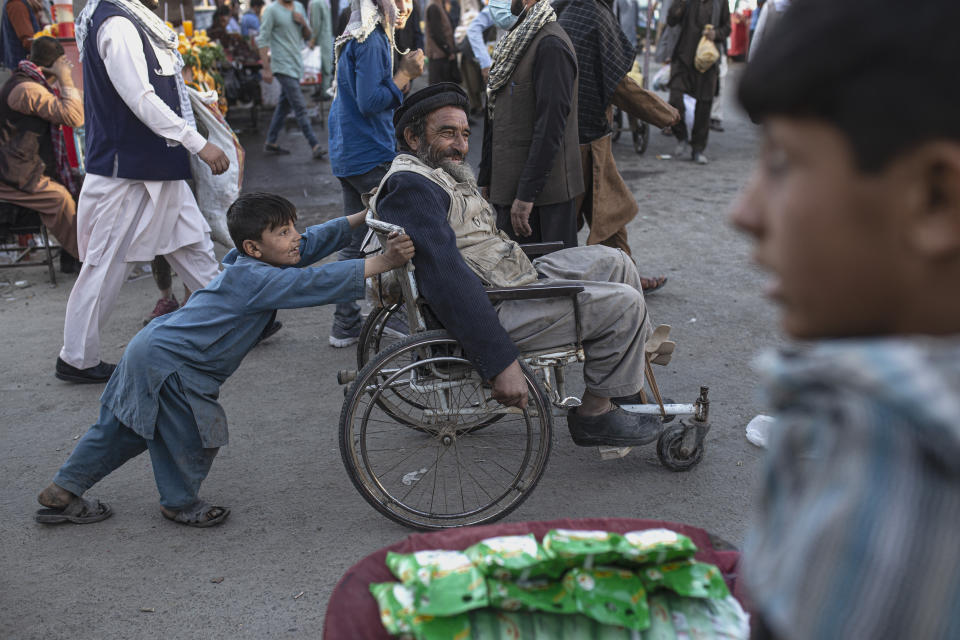 A boy pushes a man in a wheelchair trough a market in Kabul, Afghanistan, Tuesday, Oct. 12, 2021. (AP Photo/Ahmad Halabisaz)