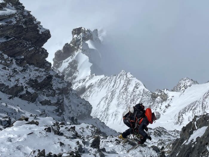 The climber on a vertiginous rock and ice ridge, partially covered in clouds