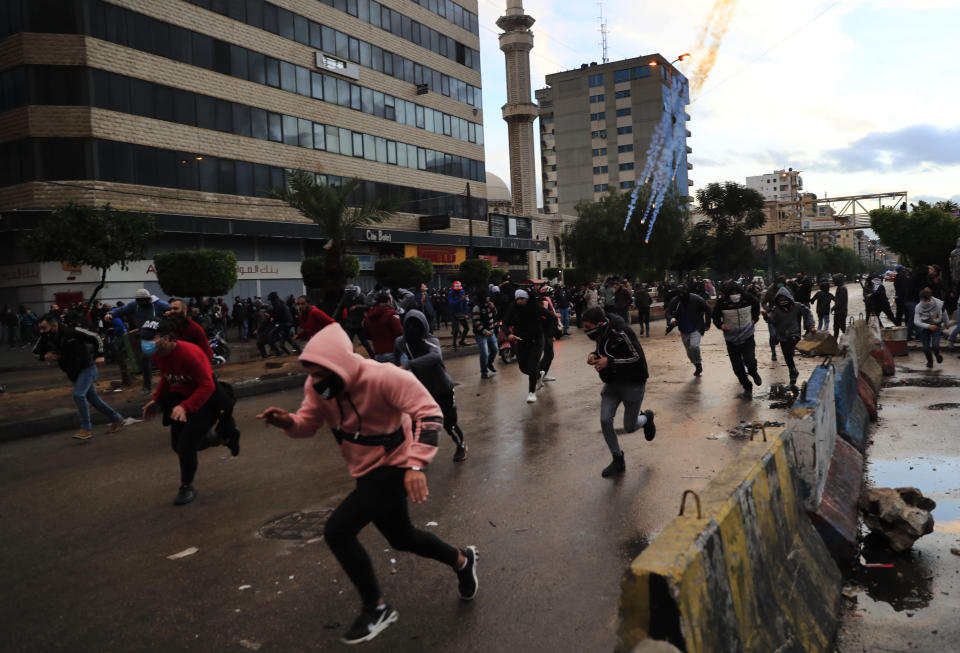 Protesters run from tear gas canisters during a protest against deteriorating living conditions and strict coronavirus lockdown measures, in Tripoli, north Lebanon, Thursday, Jan. 28, 2021. Violent confrontations for three straight days between protesters and security forces in northern Lebanon left a 30-year-old man dead and more than 220 people injured, the state news agency said Thursday. (AP Photo/Hussein Malla)