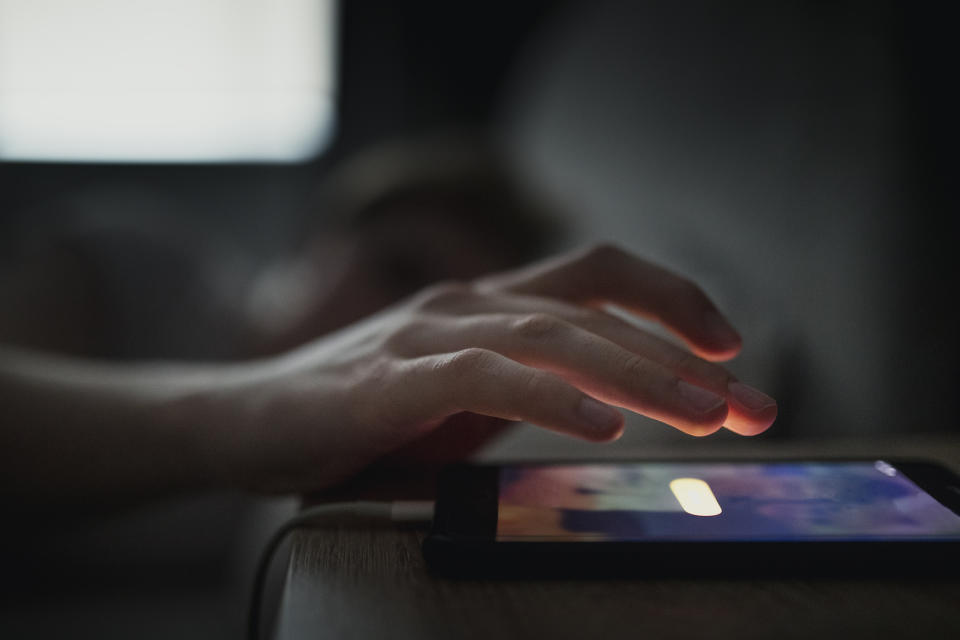 Person's hand reaching to turn off alarm on a smartphone, with a blurred background and a dimly lit environment