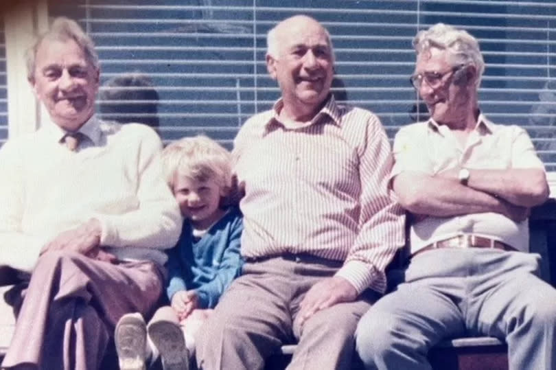 Cyril Horry, centre, in later years, with brothers Alf and Fred and Alf's son Bryan, sitting on bench in sun smiling with shirt on