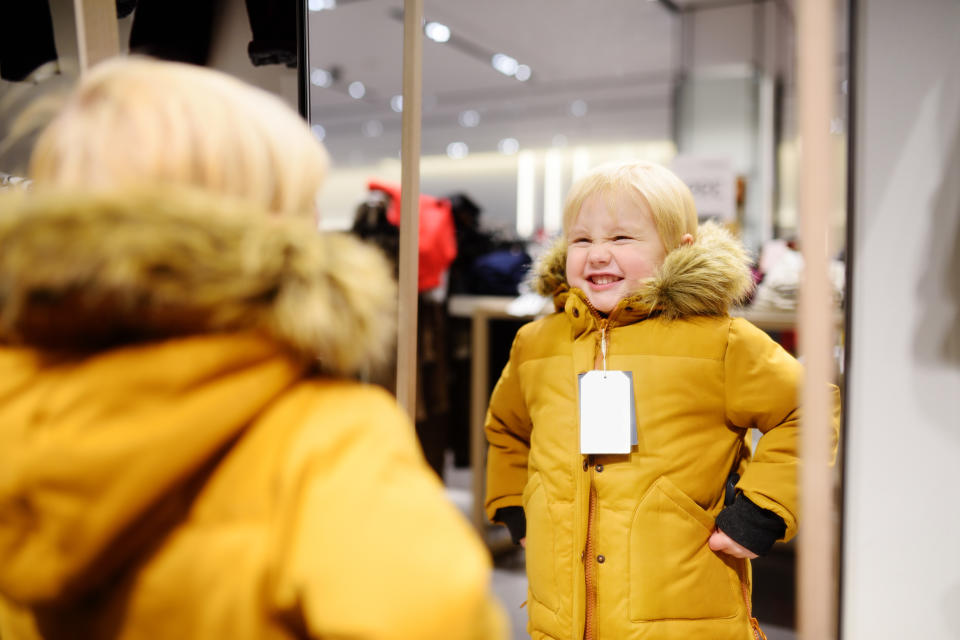 A reflection in a mirror of a boy trying on a coat.