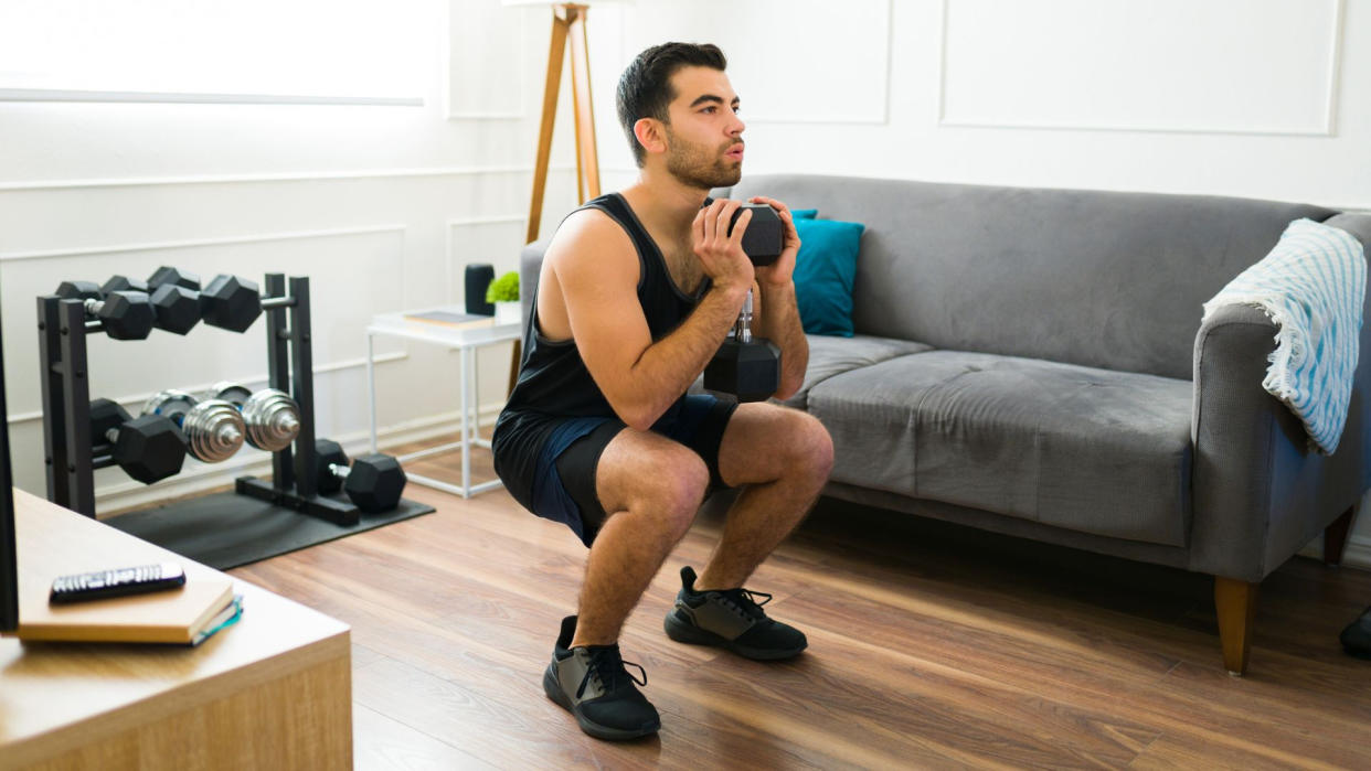  A man performing a goblet squat during a strength training workout at home . 