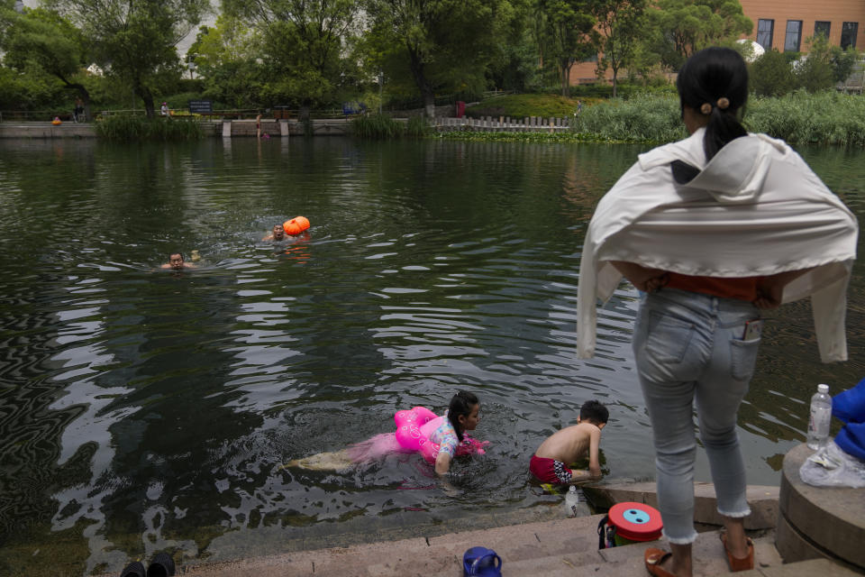 Residents cool off from an unseasonably hot day at an urban waterway in Beijing, Monday, July 3, 2023. Heavy flooding has displaced thousands of people around China as the capital had a brief respite from sweltering heat. Beijing reported 9.8 straight days when the temperature exceeded 35 C (95 F), the National Climate Center said Monday. (AP Photo/Andy Wong)