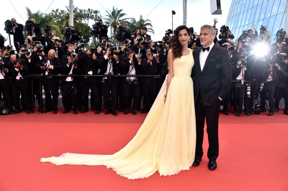 Amal Clooney porte une robe asymétrique jaune et est accompagnée par son mari George Clooney, vêtu d'un smoking