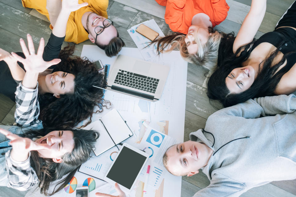 Millennials corporate life. Young people lying on the floor around working materials, relaxing, having fun during short break.