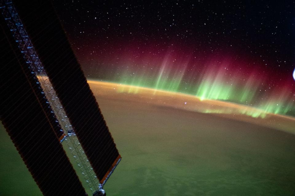 aurora green stripes on the horizon against the starry background of outer space with shadowy space station solar panels in the foreground