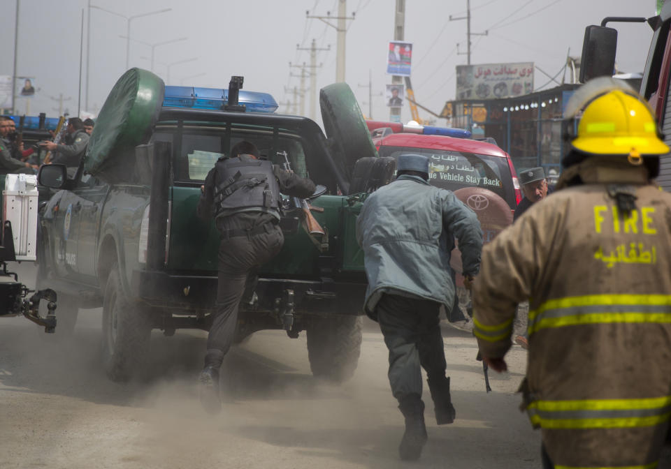 Afghan policemen run to jump on their car as Taliban militants attacked the main Afghan election commission's headquarters on the outskirts of Kabul, Afghanistan, firing on the compound with rocket-propelled grenades and heavy machine guns from a house outside its perimeter wall, Saturday, March 29, 2014. Dozens of employees and other people who had been inside the Independent Election Commission compound took cover in the basement, and no casualties were reported. But two warehouses were hit and set on fire, witnesses said. (AP Photo/Anja Niedringhaus)