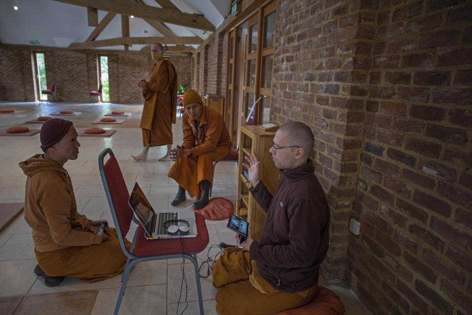 Los monjes Ajahn Kongrit, derecha, Tan Jalito, izquierda, y Tan Narindo analizan la logística del streaming en vivo de la ceremonia del Día de la Luna desde el templo budista Amvrati cerrado al público debido a la pandemia, en Great Gaddesden, Inglaterra, 28 de junio de 2020. (AP Foto/Elizabeth Dalziel)