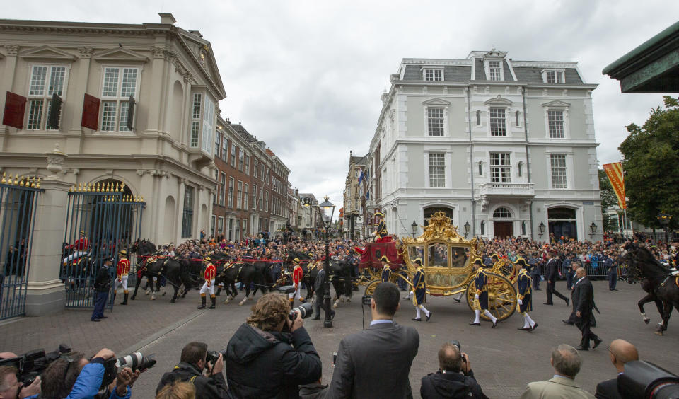 FILE- Footmen walk alongside the Golden Carriage as Netherlands' King Willem-Alexander and Queen Maxima arrive at Noordeinde Palace, after the King officially opened the new parliamentary year in The Hague, Netherlands, Tuesday Sept. 17, 2013. The Dutch king ruled out Thursday, Jan. 13, 2022, using in the near future the royal family's Golden Carriage, one side of which is decorated with a painting, center, that has drawn fire from critics who say it glorifies the Netherlands' colonial past, including its role in the global slave trade. (AP Photo/Peter Dejong, File)