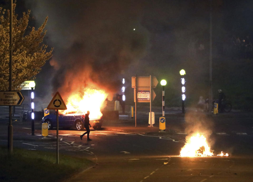 A man walks past a burning car that was hijacked by Loyalists at the Cloughfern roundabout in Newtownabbey, Belfast, Northern Ireland, Saturday April 3, 2021. Masked men threw petrol bombs and hijacked cars in the Loyalist area North of Belfast. Loyalists and unionists are angry about post-Brexit trading arrangements which they claim have created barriers between Northern Ireland and the rest of the UK. (Peter Morrison/PA via AP)