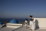 Cinzia Sansone and her daughter Josephine, from Trieste, Italy, pose for photos on a rooftop overlooking the Catholic Monastery of St. Catherine on the Greek island of Santorini on Tuesday, June 14, 2022. (AP Photo/Petros Giannakouris)