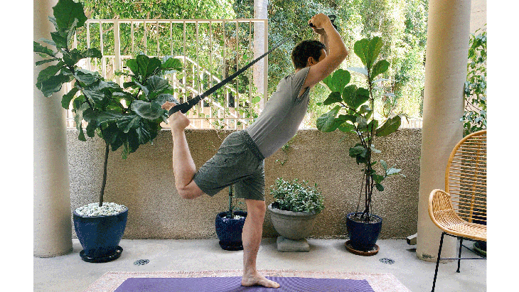 Man standing on a rug balancing on one leg using a strap to life the back knee