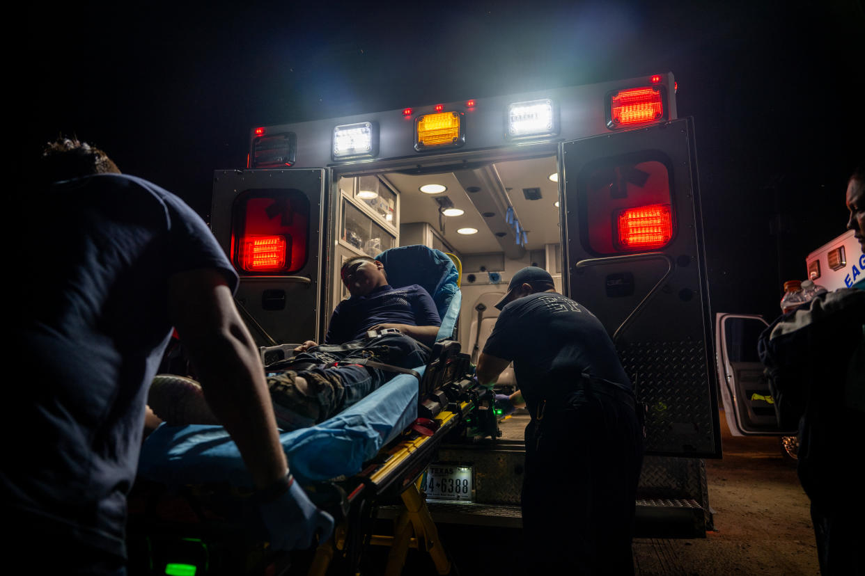Paramedics move a young boy on a stretcher into an ambulance at night.
