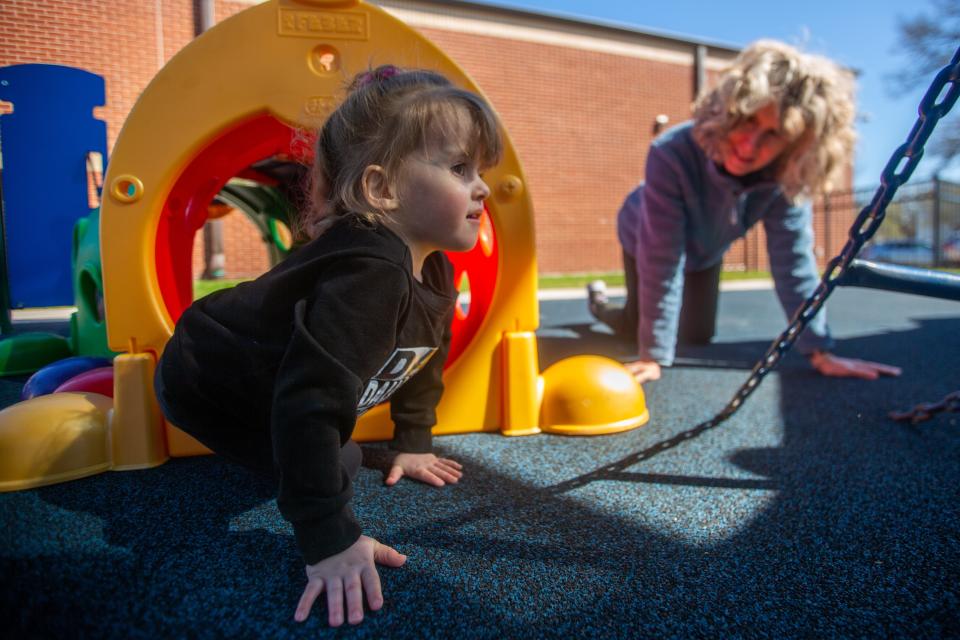 Topeka USD 501 physical therapist assistant Jenn Rollins crawls along with preschooler Amira Payne as they explore the accessible playground at Quinton Heights Education Center. The district will soon replace several elementary school playgrounds with similar playscapes as Quinton Heights'.