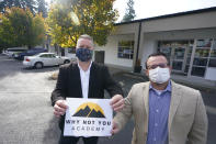 Garth Reeves, left, and Scott Canfield, co-founders of the Why Not You Academy charter school, pose for a photo with the school's new name and logo, Tuesday, Oct. 27, 2020, in front of the building that will house the school in Des Moines, Wash., south of Seattle. Seattle Seahawks NFL football quarterback Russell Wilson and his Grammy-winning wife, pop singer Ciara, are putting their money and celebrity behind rebranding the charter school, which advocates hope will boost the troubled Washington state charter school sector that has suffered from enrollment problems after years of legal challenges. (AP Photo/Ted S. Warren)