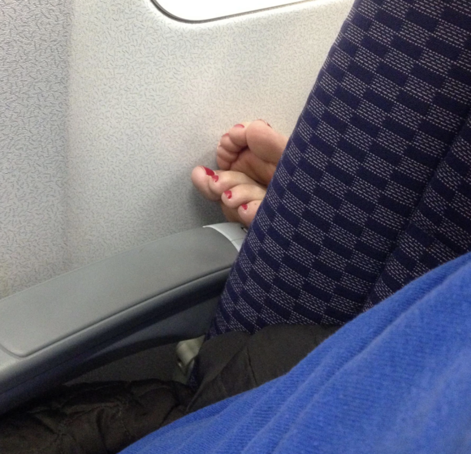 A woman's feet is perched on a stranger's armrest