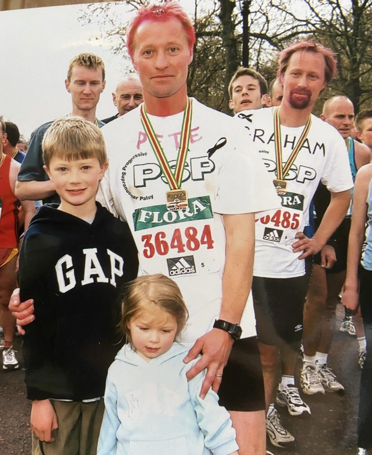 Man standing with a little boy, little girl and another man is making a face in the background