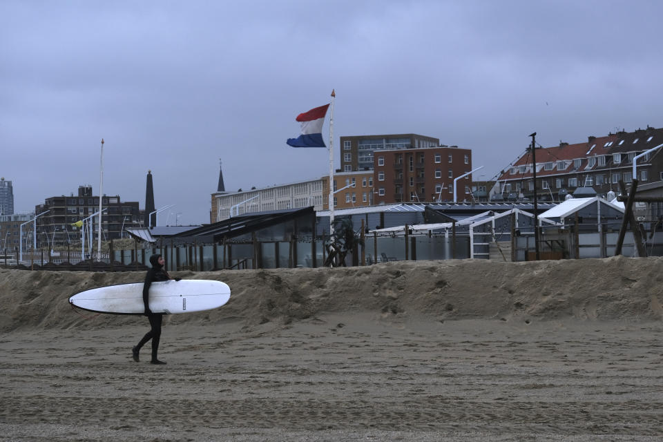 A surfer walks past a beach bar that has been protected with sand walls from approaching storm Eunice at Scheveningen, the Netherlands, on Friday Feb. 18, 2022. The Netherlands and other western European nations were bracing for the second powerful storm in three days. (AP PHOTO/Mike Corder)